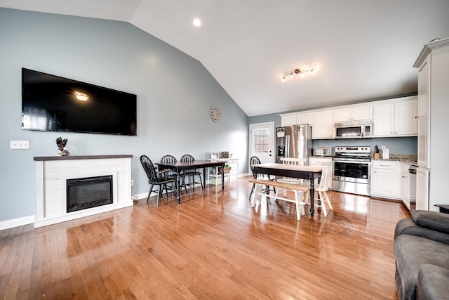 kitchen featuring open floor plan, light wood-type flooring, lofted ceiling, and appliances with stainless steel finishes