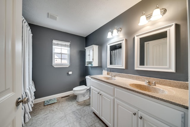 bathroom featuring a sink, toilet, double vanity, and a textured ceiling