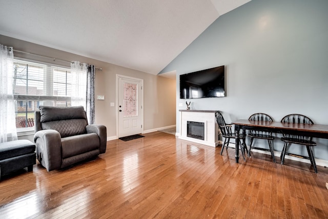 living room with a glass covered fireplace, high vaulted ceiling, baseboards, and hardwood / wood-style floors