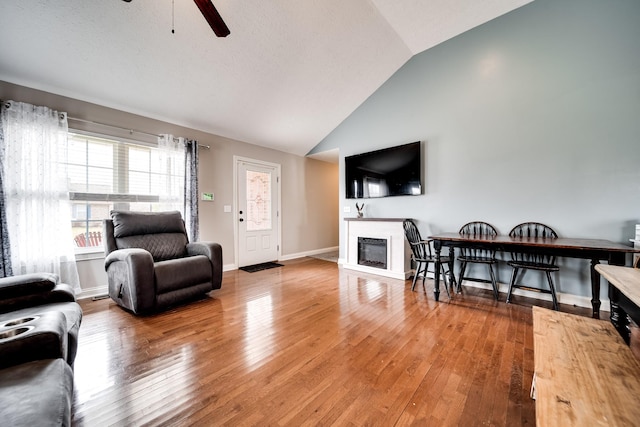 living area featuring a glass covered fireplace, wood-type flooring, vaulted ceiling, and a ceiling fan