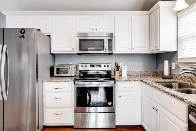kitchen with light stone counters, a toaster, white cabinets, appliances with stainless steel finishes, and a sink