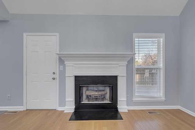 interior details featuring visible vents, a fireplace with flush hearth, baseboards, and wood finished floors