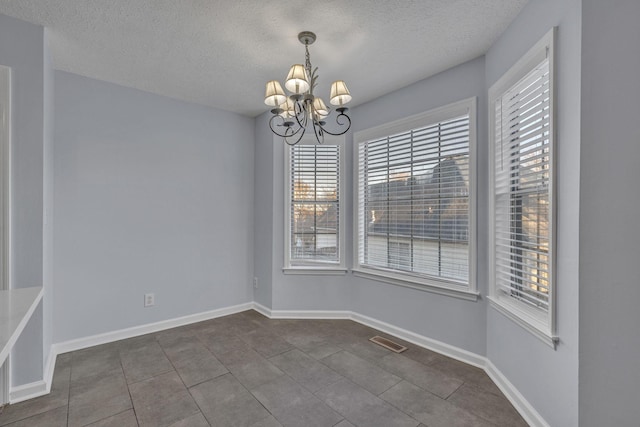 unfurnished dining area with visible vents, a notable chandelier, dark tile patterned floors, a textured ceiling, and baseboards
