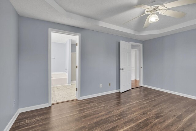 unfurnished bedroom featuring baseboards, a raised ceiling, a textured ceiling, and wood finished floors