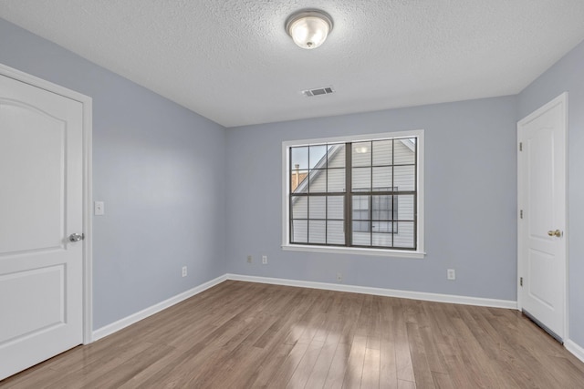 empty room with visible vents, baseboards, a textured ceiling, and wood finished floors
