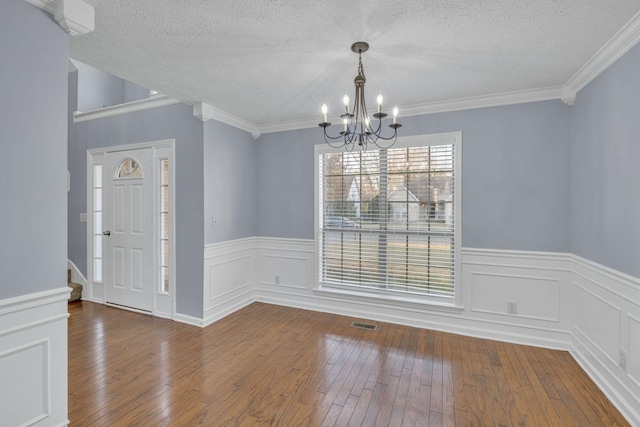 unfurnished dining area featuring visible vents, ornamental molding, hardwood / wood-style floors, an inviting chandelier, and a textured ceiling