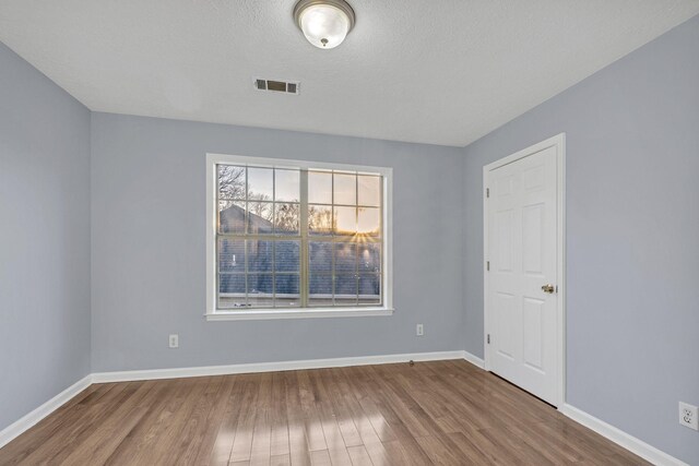 unfurnished room featuring visible vents, wood finished floors, baseboards, and a textured ceiling