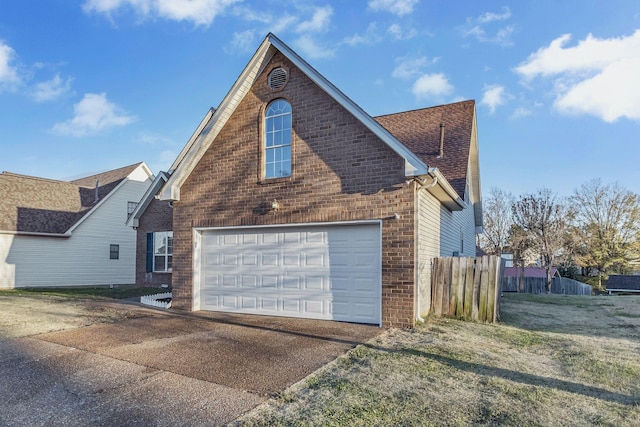 view of property exterior featuring brick siding, a shingled roof, concrete driveway, and fence