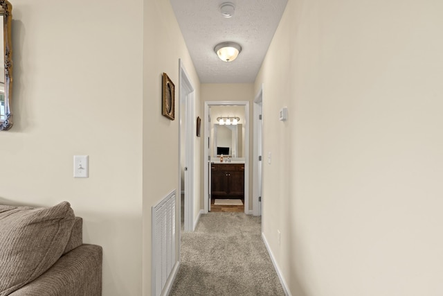 hall featuring baseboards, light colored carpet, visible vents, and a textured ceiling