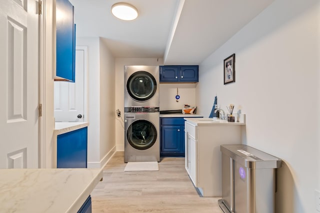 washroom with a sink, cabinet space, stacked washing maching and dryer, and light wood-type flooring