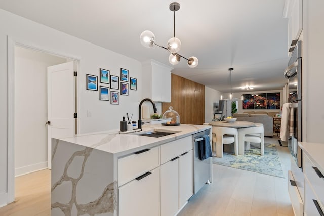 kitchen with a sink, white cabinets, light stone countertops, stainless steel dishwasher, and decorative light fixtures