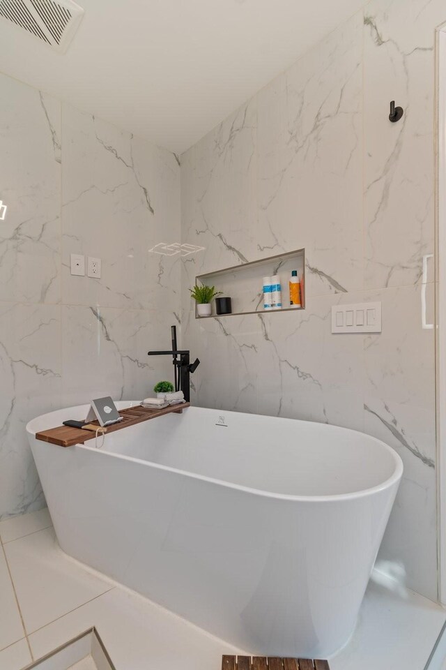 bathroom with stone wall, visible vents, and a freestanding tub
