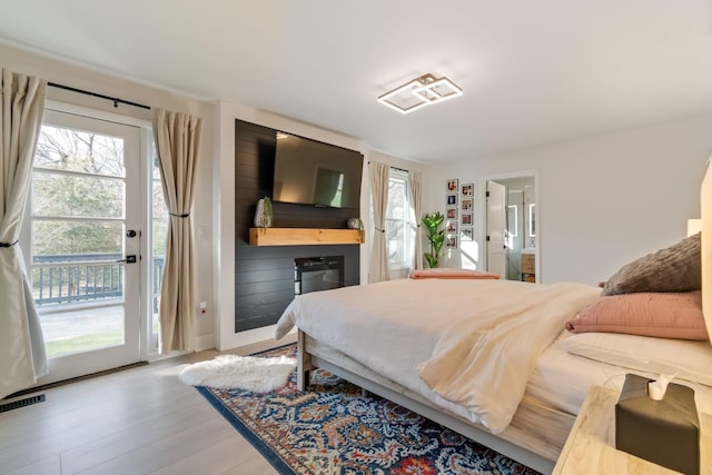 bedroom with ensuite bath, access to exterior, visible vents, and wood finished floors