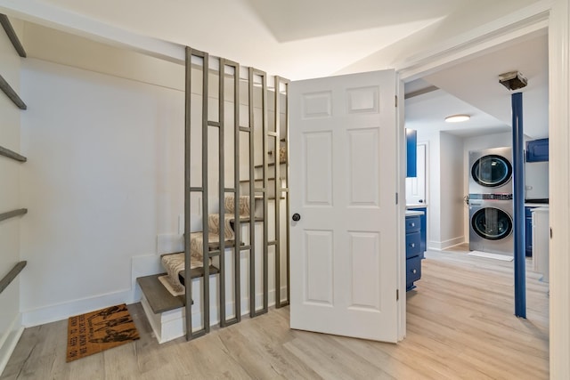 interior space featuring baseboards, light wood-style floors, stacked washer / dryer, and stairs