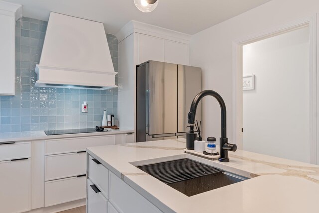 kitchen with decorative backsplash, white cabinetry, black electric stovetop, custom range hood, and freestanding refrigerator