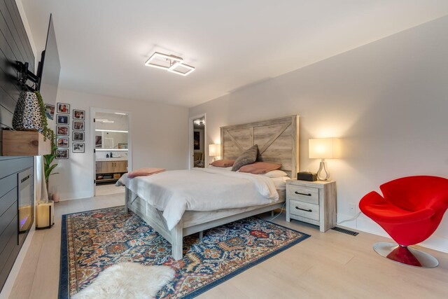 bedroom with connected bathroom, visible vents, and wood finished floors