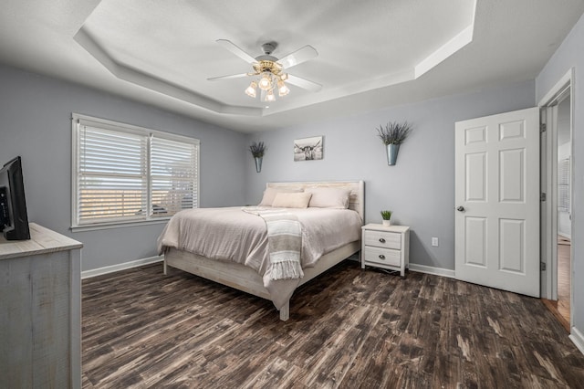 bedroom featuring baseboards, dark wood-type flooring, and a tray ceiling