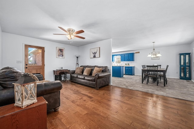 living area with baseboards, hardwood / wood-style floors, and ceiling fan with notable chandelier