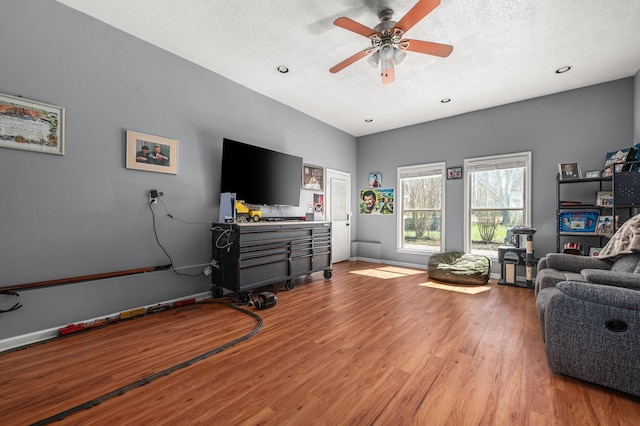 living area featuring baseboards, light wood-style floors, a ceiling fan, and a textured ceiling