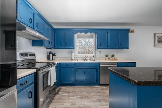 kitchen with light wood-type flooring, under cabinet range hood, blue cabinetry, a sink, and stainless steel appliances