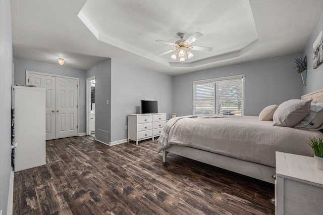 bedroom with ceiling fan, baseboards, wood finished floors, a closet, and a raised ceiling