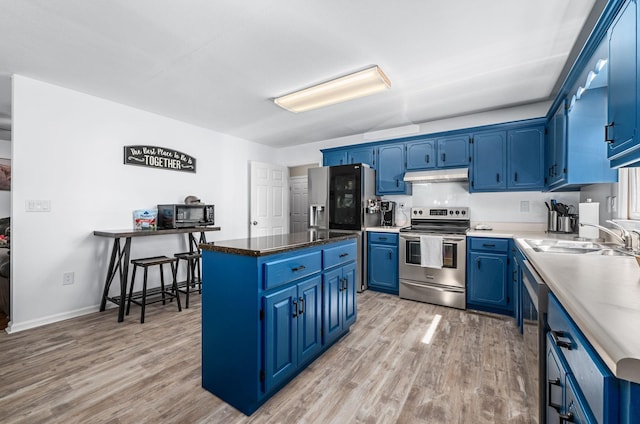 kitchen featuring blue cabinets, light wood-style flooring, under cabinet range hood, a sink, and appliances with stainless steel finishes