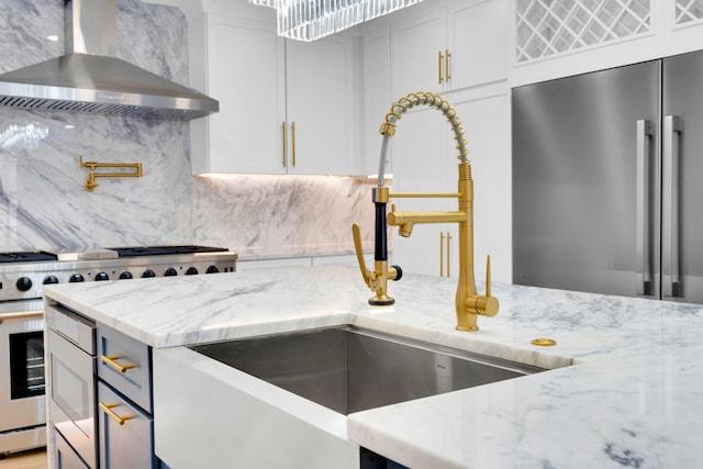 kitchen with a sink, premium appliances, wall chimney range hood, decorative backsplash, and light stone countertops