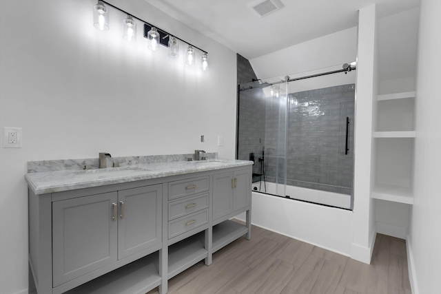 bathroom featuring wood finished floors, visible vents, combined bath / shower with glass door, and a sink