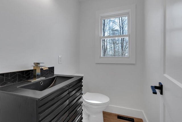 half bathroom with vanity, wood finished floors, visible vents, baseboards, and toilet