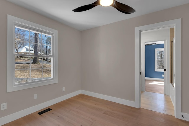empty room featuring light wood-style flooring, a ceiling fan, visible vents, and baseboards
