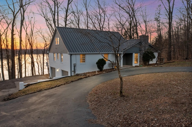 view of front facade featuring driveway, a chimney, a standing seam roof, and metal roof