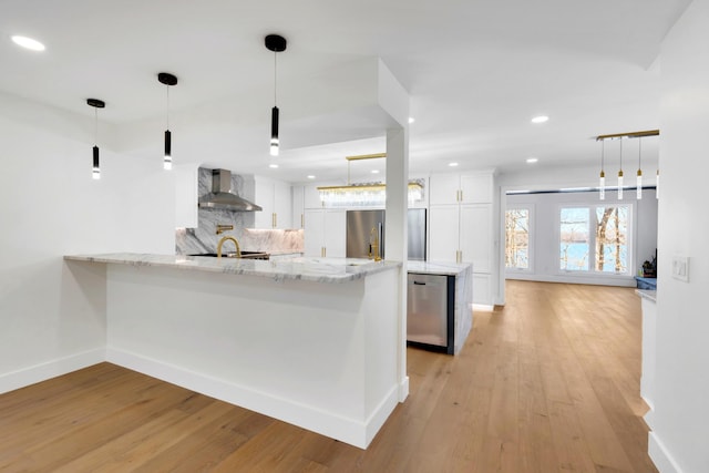 kitchen featuring tasteful backsplash, a peninsula, stainless steel appliances, white cabinetry, and wall chimney exhaust hood