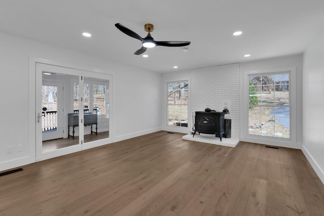 unfurnished living room with a wood stove, wood finished floors, visible vents, and a healthy amount of sunlight