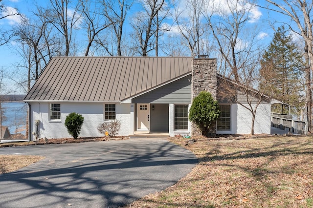 view of front of house with a standing seam roof, aphalt driveway, metal roof, brick siding, and a chimney