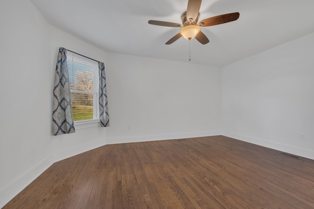 empty room with dark wood-style floors, visible vents, baseboards, and ceiling fan