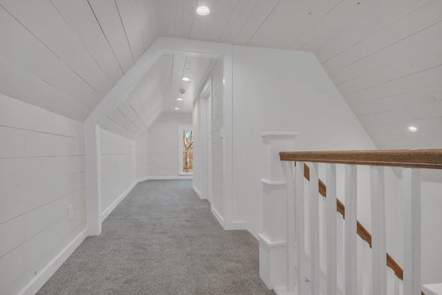 hall with an upstairs landing, wooden ceiling, carpet flooring, and vaulted ceiling