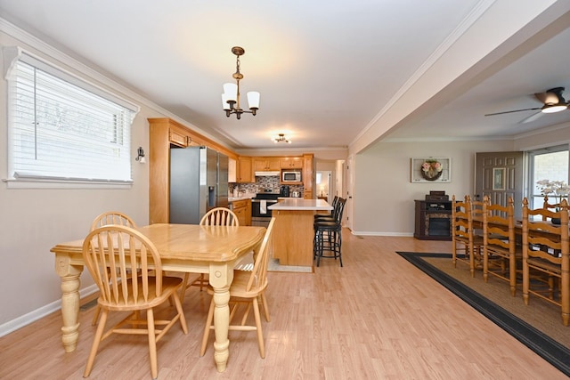dining space with ceiling fan with notable chandelier, light wood-type flooring, crown molding, and baseboards