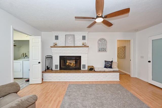 living area featuring a textured ceiling, wood finished floors, a fireplace, ceiling fan, and washing machine and clothes dryer