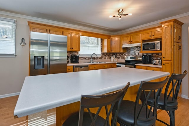 kitchen featuring a sink, decorative backsplash, stainless steel appliances, under cabinet range hood, and light wood-type flooring