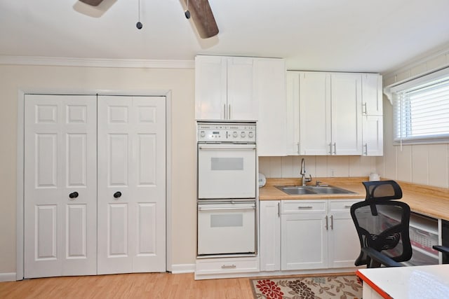 kitchen with light wood-style flooring, a sink, light countertops, white cabinets, and double oven