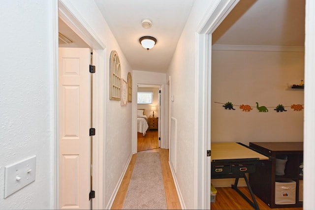 corridor featuring baseboards, light wood-style floors, and ornamental molding
