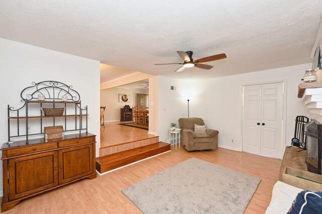 living room featuring light wood-type flooring, a textured ceiling, ceiling fan, and a fireplace