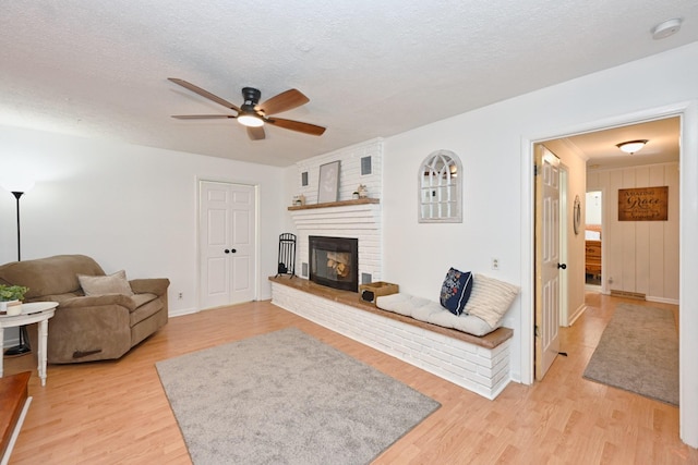 living room featuring a textured ceiling, a fireplace, a ceiling fan, and light wood finished floors