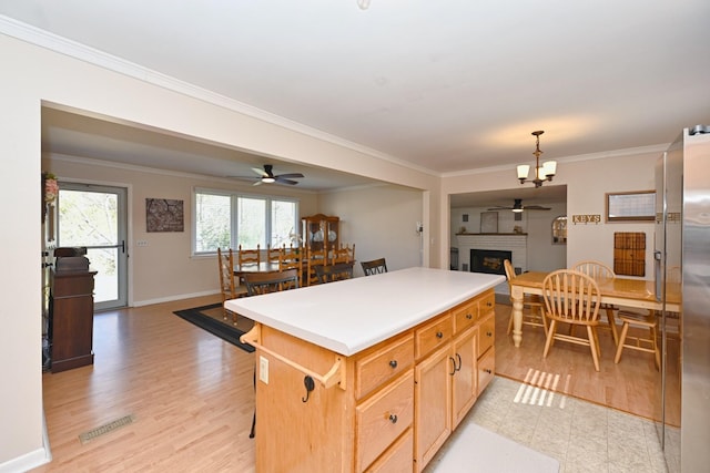 kitchen featuring ornamental molding, a kitchen island, open floor plan, baseboards, and a brick fireplace