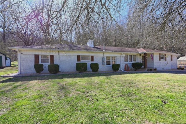 ranch-style home featuring brick siding, an outbuilding, a chimney, and a front yard