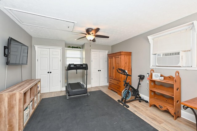 exercise room featuring cooling unit, wood finished floors, a ceiling fan, baseboards, and attic access