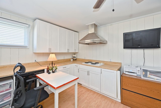 kitchen with light wood finished floors, ceiling fan, white cabinetry, wall chimney exhaust hood, and white cooktop