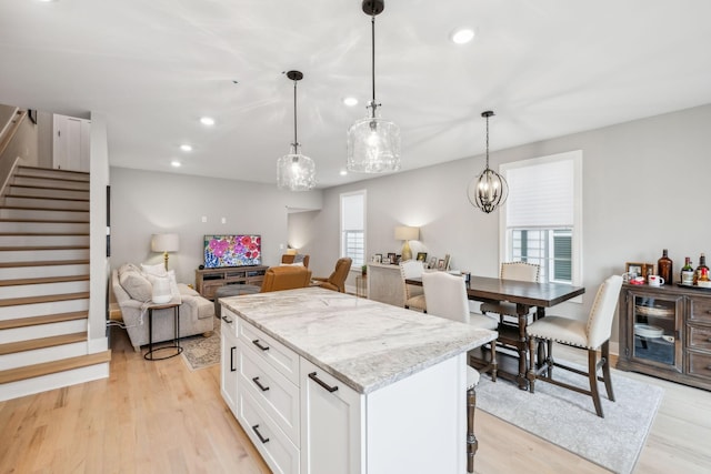 kitchen featuring white cabinetry, light stone countertops, a center island, open floor plan, and light wood-type flooring