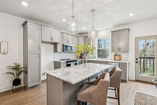 kitchen featuring gray cabinets, stainless steel appliances, a center island, a sink, and light stone countertops