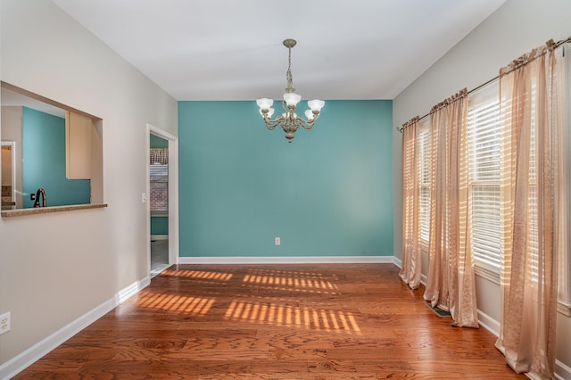 unfurnished dining area with an inviting chandelier, wood finished floors, baseboards, and a sink